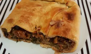 Una fetta di pizza di scarola, con ripieno di verdure e olive, su un piatto a righe bianche e nere.