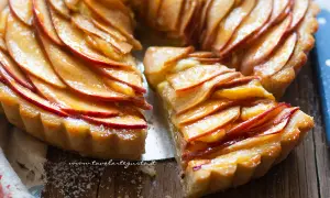 Una fetta di crostata di mele dorata, con mele caramellate disposte a spirale su una base friabile.