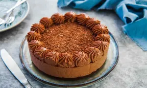 Delizioso cheesecake al cioccolato con decorazioni a ciuffi e scaglie di cioccolato. Un coltello da burro è pronto per essere usato.