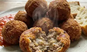 Polpette al forno dorate e croccanti, una aperta rivela un interno succulento. Servite con salsa rossa e pane.