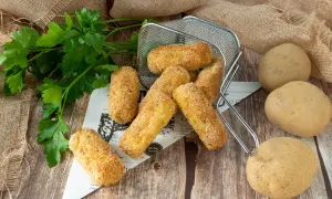Crocchette di patate in friggitrice ad aria, dorate e croccanti, pronte per essere gustate. Accanto, patate fresche e prezzemolo.