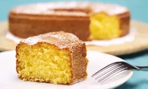 Una fetta di torta 7 vasetti soffice e dorata, spolverata di zucchero a velo, su un piatto bianco con una forchetta.