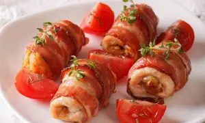 Involtini di pollo avvolti in pancetta croccante, guarniti con timo fresco e serviti con spicchi di pomodoro.