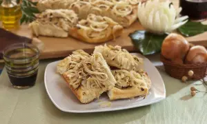 Focaccia con cipolle dorate, fragrante e invitante, servita su un piatto bianco. Sullo sfondo, ingredienti freschi e una bottiglia d'olio.
