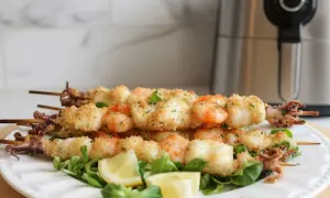 Spiedini di gamberi e calamari impanati, cotti alla perfezione nella friggitrice ad aria. Serviti su un letto di insalata con spicchi di limone.