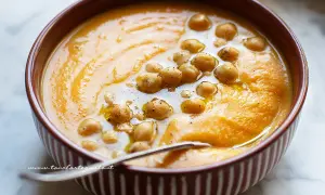 Un cremoso passato di verdure arancione, guarnito con ceci e un filo d'olio. Perfetto per una cena confortante.