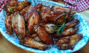 Alette di pollo al forno dorate e succulente, servite su un piatto decorato con un rametto di rosmarino.