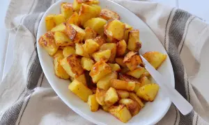 Un piatto bianco pieno di patate al forno dorate e croccanti, pronte per essere gustate.