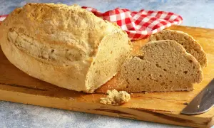 Pane casereccio con lievito istantaneo, tagliato su un tagliere di legno, con un tovagliolo a quadri rossi e bianchi.