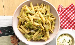 Penne con carciofi, un piatto che Antonino Cannavacciuolo saprebbe preparare alla perfezione, servito in una ciotola rosa.