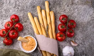 Grissini fatti in casa dorati, con pomodorini freschi, aglio e una salsa cremosa. Perfetti per un aperitivo rustico.