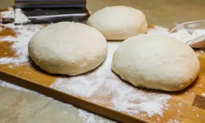 Tre panetti soffici di pizza a lunga lievitazione, pronti per essere stesi su un tagliere di legno infarinato.