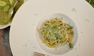 Un piatto di pasta condita con un cremoso macco di fave fresche, guarnito con aneto e formaggio grattugiato.