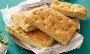 Focaccia con lievito istantaneo, dorata e soffice, guarnita con erbe aromatiche e sale grosso. Perfetta per un pasto veloce e gustoso.