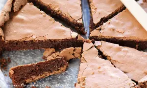 Una deliziosa torta al cioccolato fondente, tagliata a fette triangolari, con una crosta leggermente screpolata e un interno umido e invitante.