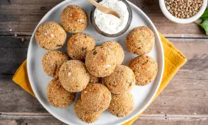 Piatto di polpette di lenticchie dorate e croccanti, servite con una ciotolina di salsa cremosa e un cucchiaino di legno.