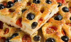Focaccia pugliese ricetta originale sofficissima, con pomodorini e olive nere, condita con erbe aromatiche.