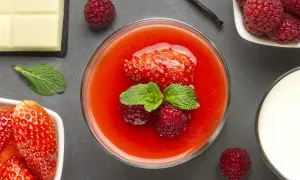 Un bicchiere di coulis di fragole con fragola, lamponi e menta. Accanto, cioccolato bianco, lamponi freschi e un bicchiere di latte.
