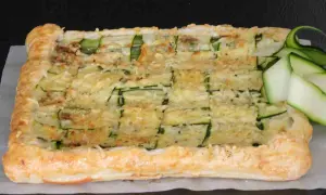 Torta salata con pasta sfoglia e zucchine, gratinata al forno e guarnita con fettine di zucchina fresca.