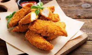Bocconcini di pollo in friggitrice ad aria, dorati e croccanti, serviti con basilico fresco e salsa.