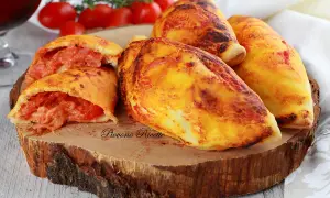 Panzerotti al forno dorati e ripieni di pomodoro e formaggio filante, serviti su un tagliere di legno.