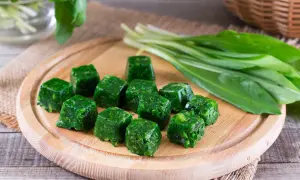 Cubetti di spinaci surgelati in padella, pronti per essere cucinati. Accanto, un mazzo di spinaci freschi.