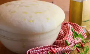 Impasto lievitato per pizza con lievito di birra, pronto per essere infornato. Olio d'oliva e peperoncini completano la scena.