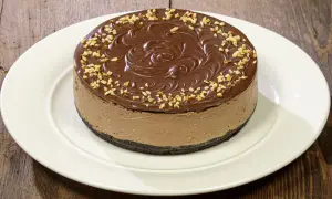 Cheesecake alla Nutella con glassa al cioccolato e nocciole tritate, su un piatto bianco.