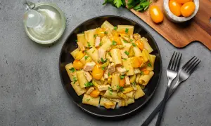 Piatto di pasta con pesce spada, pomodorini gialli e zucchine, guarnito con prezzemolo fresco.