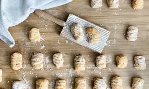 Gnocchi di zucca fatti in casa, pronti per essere cotti, sparsi su un tagliere di legno con un rigagnocchi.