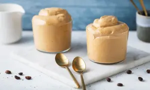 Due bicchieri di cremosa crema di caffè senza panna, perfetti per una pausa golosa. Chicchi di caffè e cucchiaini dorati completano la scena.