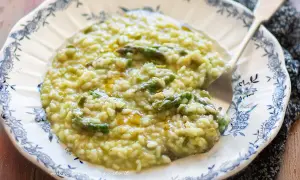 Un cremoso risotto con asparagi, servito su un piatto decorato. Un piatto primaverile che profuma di buono.