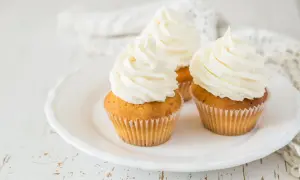 Tre cupcake su un piatto bianco, decorati con abbondante crema al burro soffice e ariosa.