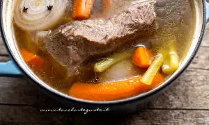 Un pezzo di carne succulenta cuoce lentamente in un brodo di carne aromatico, con carote, sedano e cipolla.