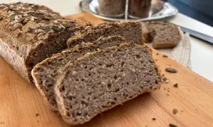 Fetta di pane di grano saraceno, cosparso di semi, su tagliere di legno.