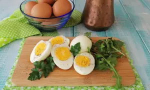 Uova sode in friggitrice ad aria, tagliate a metà, con un ciuffo di prezzemolo e rucola su un tagliere di legno.