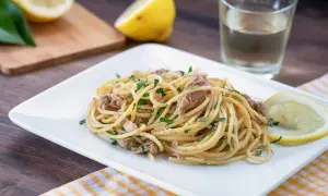 Un piatto di pasta tonno e limone, guarnito con prezzemolo fresco e spicchi di limone, pronto per essere gustato.