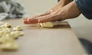 Mani che modellano impasto per creare orecchiette fatte in casa su un tagliere di legno.