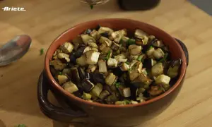 Melanzane in friggitrice ad aria, tagliate a cubetti e condite con erbe aromatiche, servite in una ciotola di terracotta.