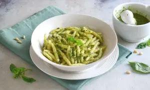 Un piatto invitante di pasta al pesto, condita con basilico fresco e pinoli, accanto a un mortaio con altro pesto.
