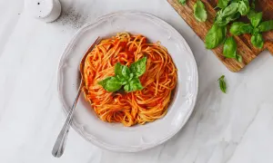 Un piatto di spaghetti al sugo di pomodorini freschi, guarnito con basilico, pronto per essere gustato.
