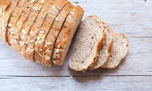 Pane fatto in casa ricetta della nonna, con crosta dorata e semi, affettato su un tavolo di legno.