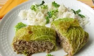 Involtini di verza ripieni di carne e riso, serviti su un piatto bianco con contorno di riso bianco e foglie di verza sminuzzate.
