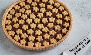 Deliziosa crostata alla nutella con decorazioni a forma di fiorellini. Un dolce che porta gioia, come dice la spatola: "Happiness is a piece of cake".