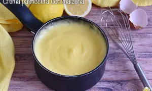 Crema pasticcera liscia e vellutata, preparata con amido di mais, pronta per farcire dolci. Accanto, limoni e frusta.