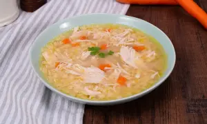 Un confortevole brodo di pollo con pezzi di pollo sfilacciato, carote e un rametto di prezzemolo.