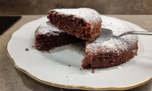 Una fetta di torta all'acqua al cacao, soffice e spolverata di zucchero a velo, viene sollevata da una spatola.