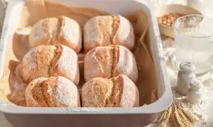 Sei panini dorati, pronti per essere cotti nel pane in friggitrice ad aria. La farina spolverata e le spighe di grano completano la scena.