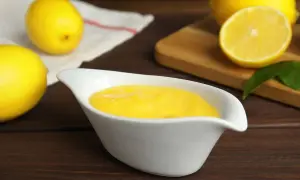 Una ciotola bianca contiene una vellutata crema al limone, con limoni freschi sullo sfondo.