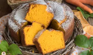 Una soffice torta di carote, cosparsa di zucchero a velo, servita in un cestino di vimini. Le fette mostrano l'interno arancione e invitante.